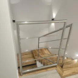 Nowoczesne schody z drewnianymi stopniami i balustradą ze stali nierdzewnej, oświetlone punktowo, widok z góry, szare panele podłogowe.