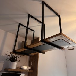 Damian Dwojakowski - Nowoczesna, podwieszana półka z drewnianymi blatami i czarną, metalową konstrukcją, zamontowana w kuchni. Widoczny fragment zabudowy kuchennej i sprzęt AGD.