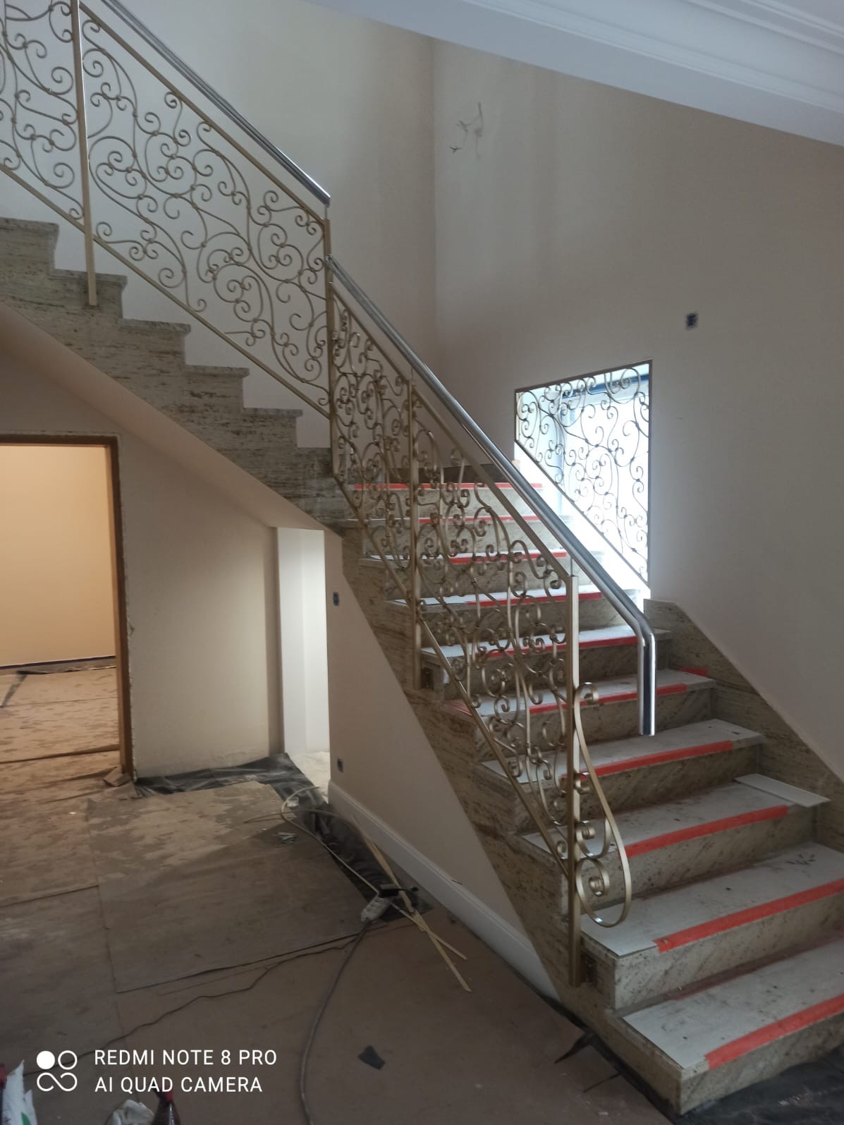 Schody z kamienia z ozdobną, metalową balustradą i poręczą. Widoczne zabezpieczenia na stopniach. Ujęcie z dołu, widok na okno z metalową kratą.