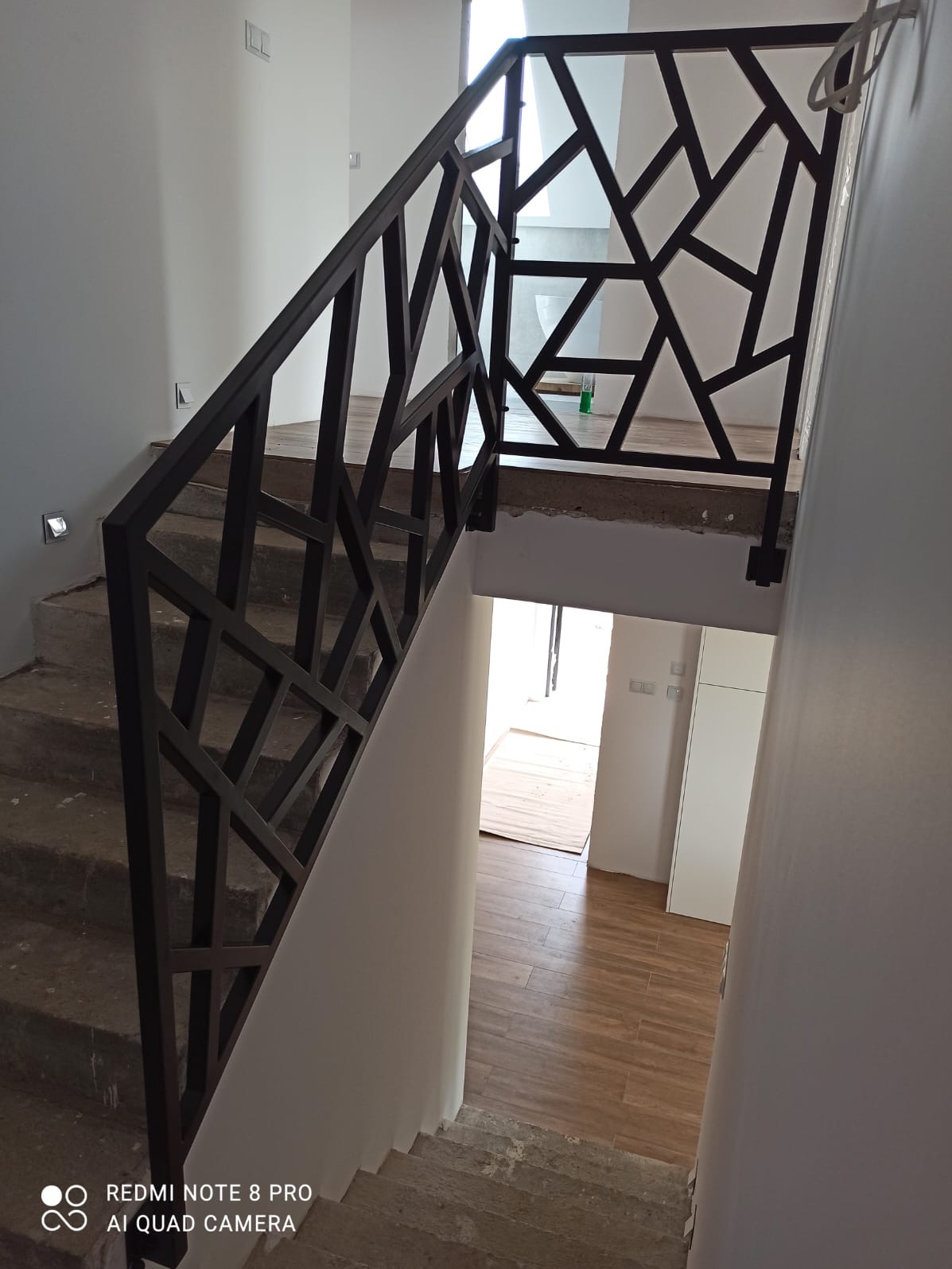 Nowoczesna poręcz schodowa z geometrycznym wzorem w Białymstoku. Ciemna, metalowa konstrukcja na jasnych schodach, widok z góry, minimalistyczny design.