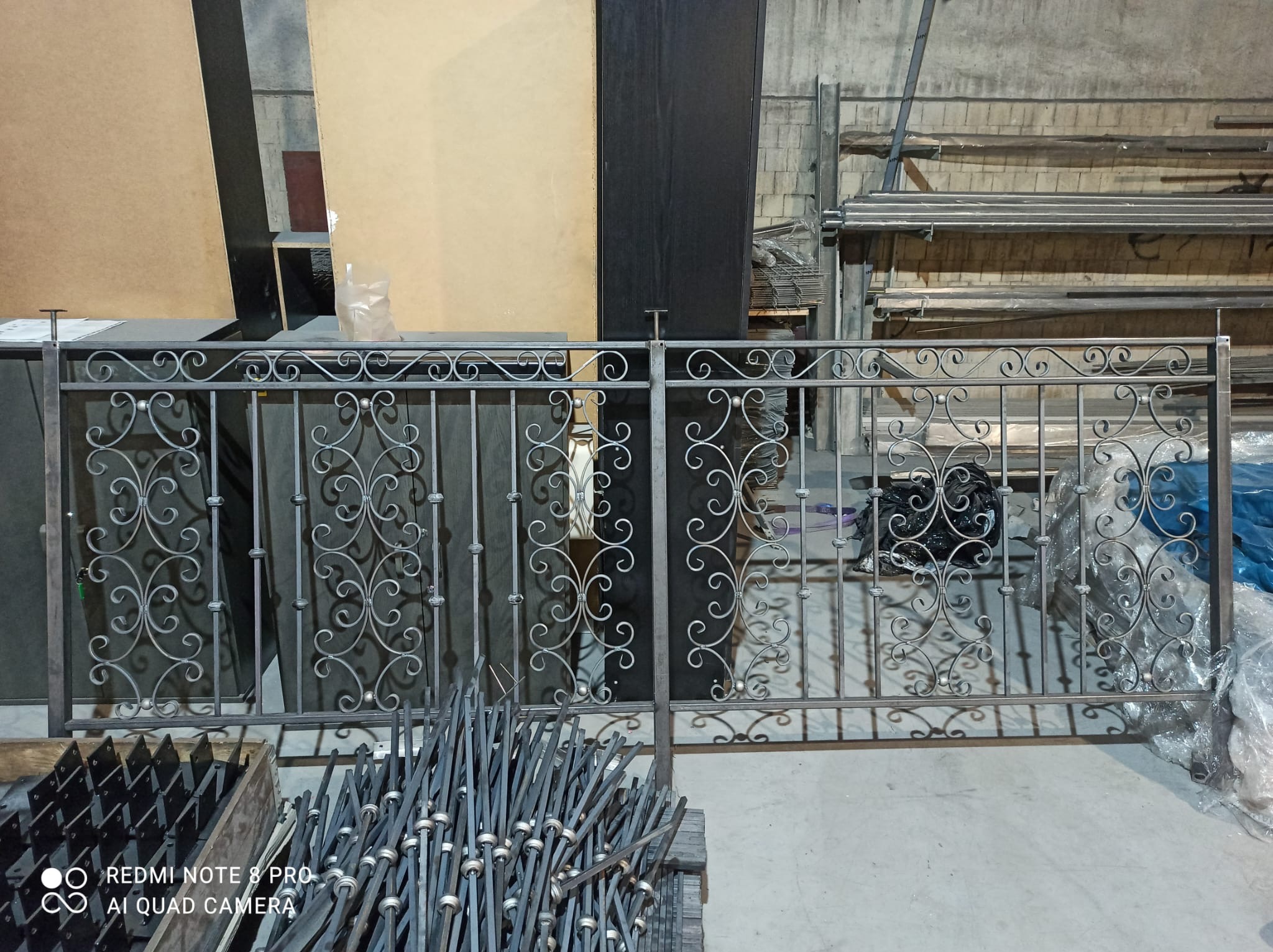 Element kutej balustrady z dekoracyjnymi zawijasami, w szarym kolorze, widoczny na tle materiałów i narzędzi w warsztacie.