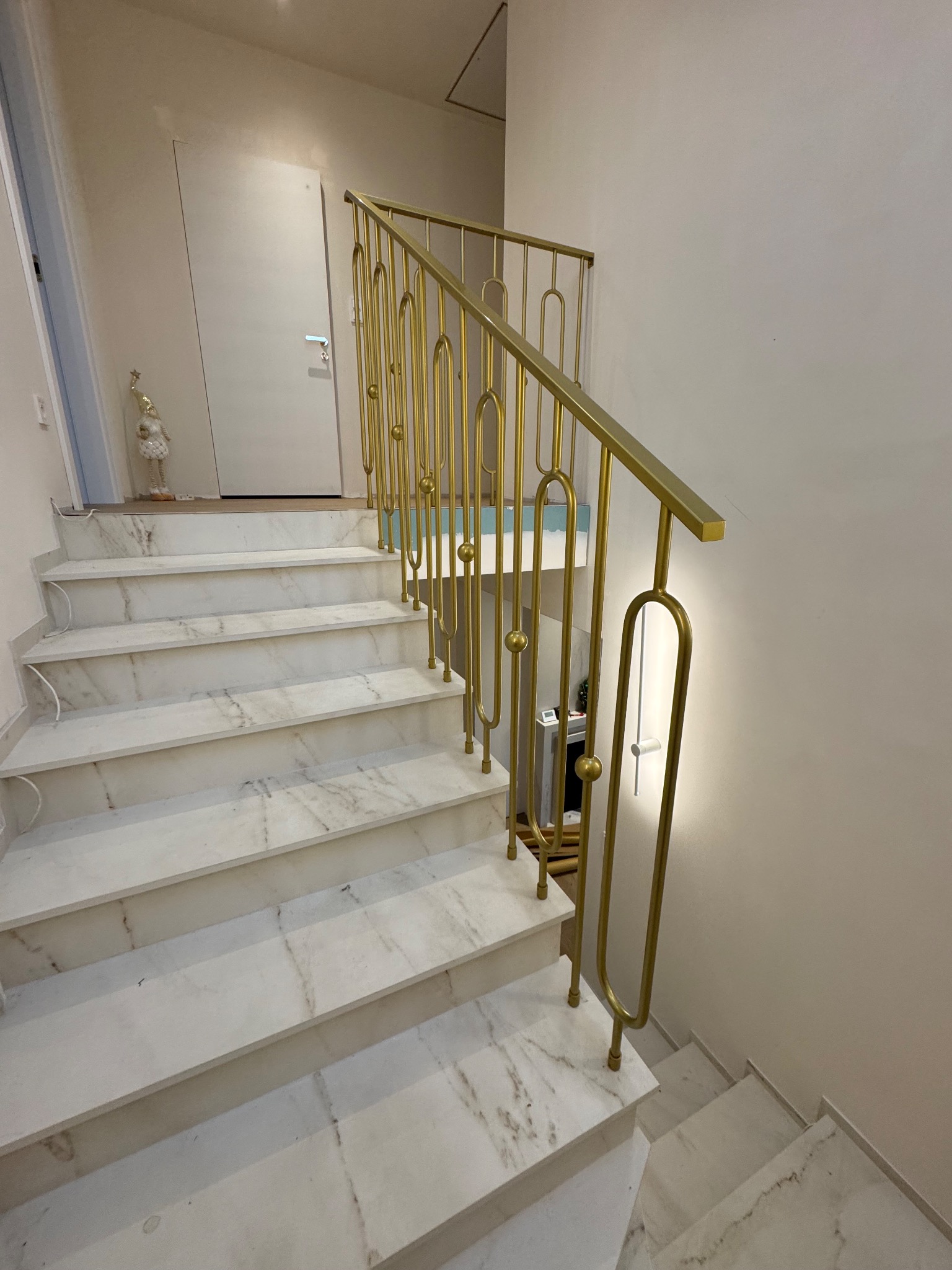 Marmurowe schody z dekoracyjną, złotą metalową balustradą w nowoczesnym stylu. Widok z dołu, oświetlenie ciepłe, wnętrze jasne.