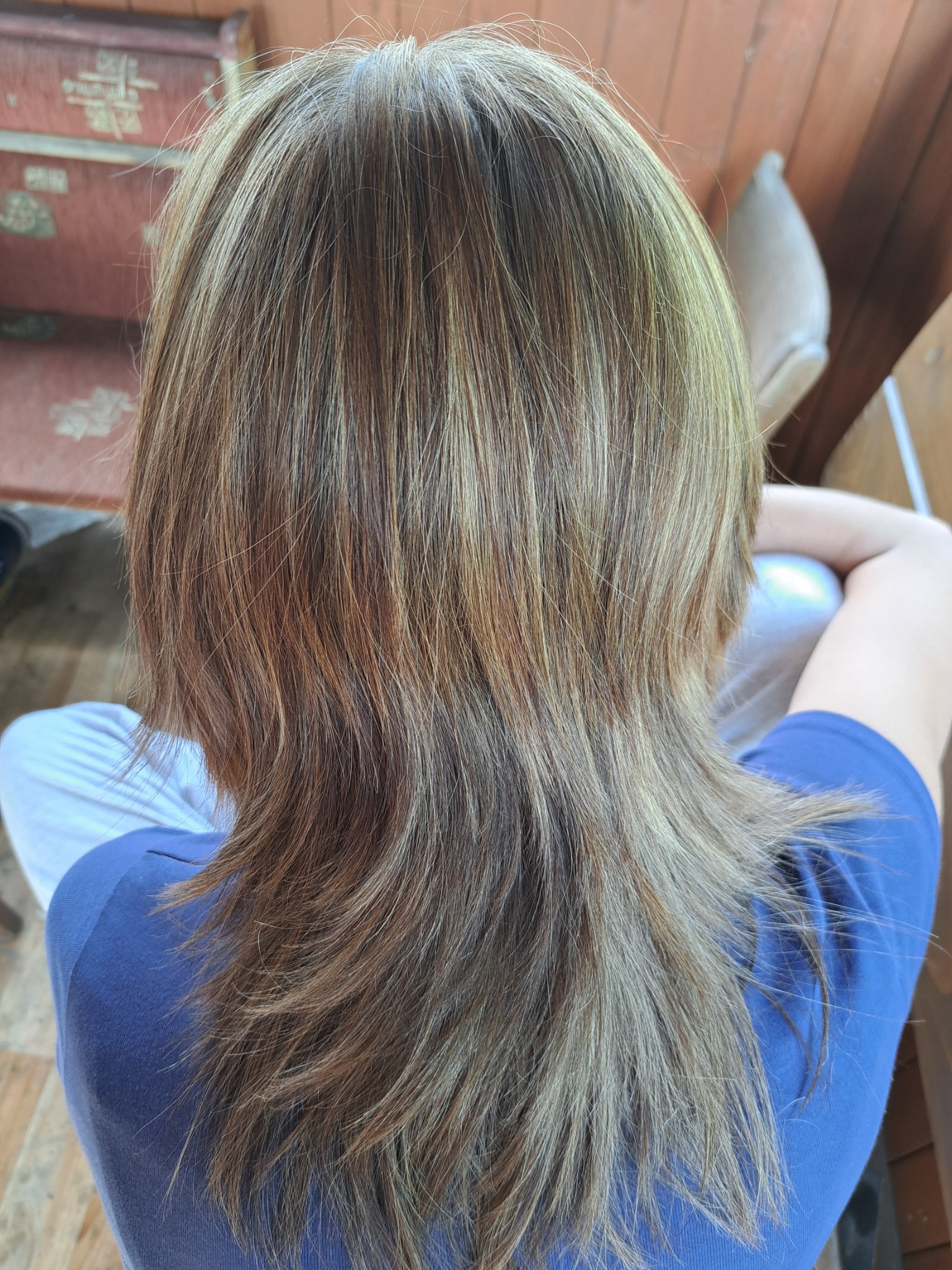 Włosy po koloryzacji z widocznymi pasemkami w odcieniach blondu i brązu, długość do ramion, widok z tyłu na tle drewnianej werandy.