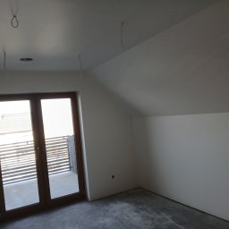 Usługi Budowlano-Remontowe Paweł Wojciechowski - Poddasze po szpachlowaniu i malowaniu ścian na biało, z widocznymi przewodami oświetleniowymi i wyjściem na balkon z drewnianą ramą okienną.