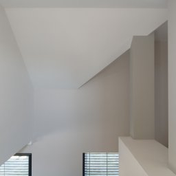 Usługi Budowlano-Remontowe Paweł Wojciechowski - Świetlik w skosie dachu po malowaniu, widok z dołu. Minimalistyczne wnętrze z oknami i jasnymi ścianami. Neutralna paleta barw.
