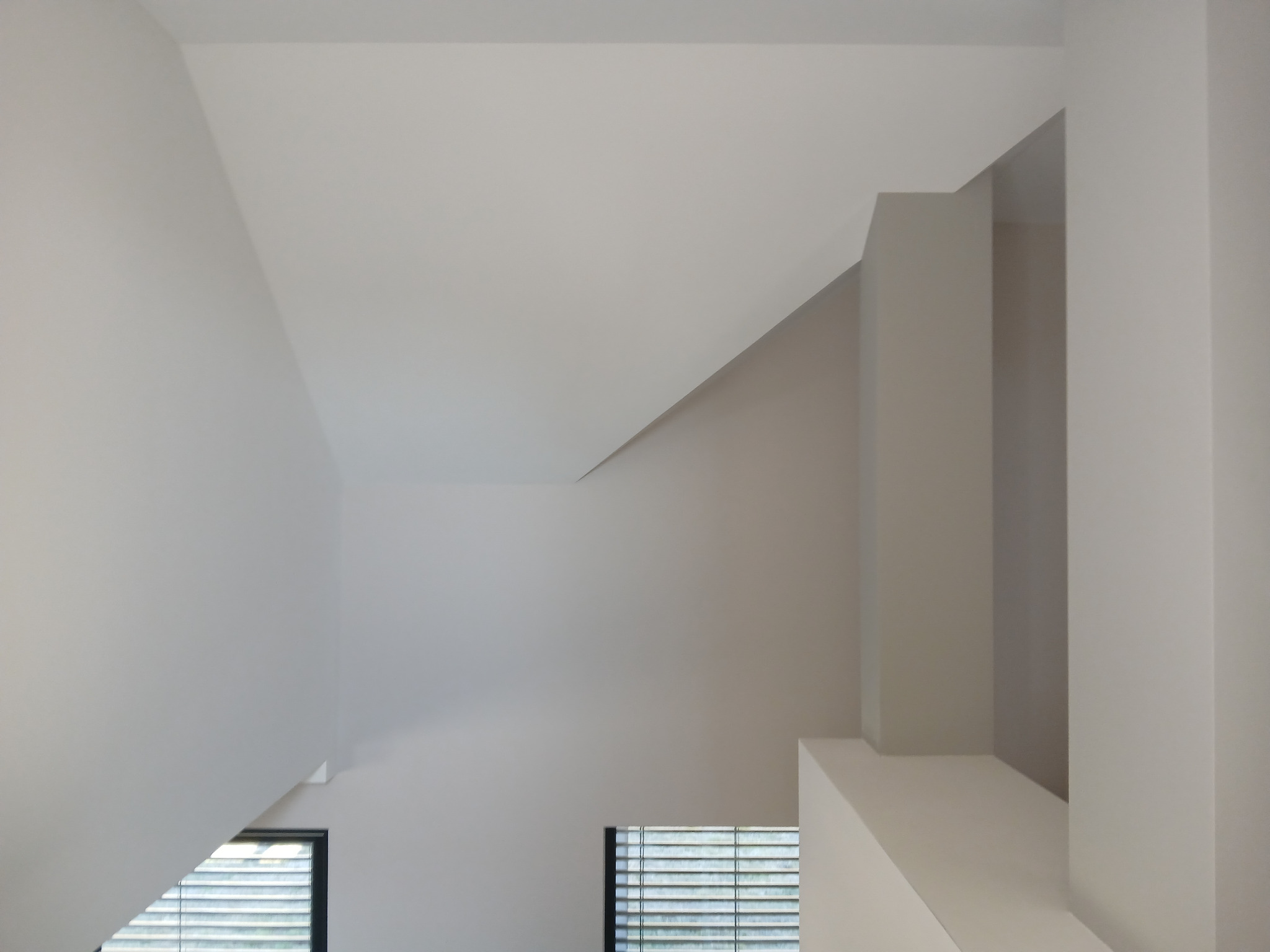 Świetlik w skosie dachu po malowaniu, widok z dołu. Minimalistyczne wnętrze z oknami i jasnymi ścianami. Neutralna paleta barw.