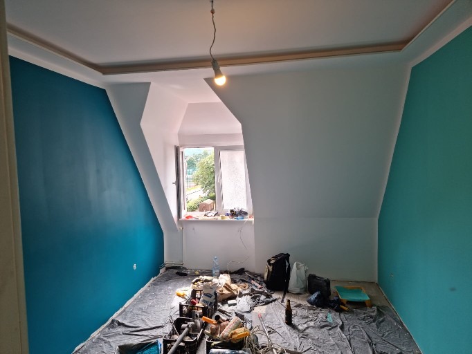 Pokój na poddaszu po malowaniu ścian na biało i turkusowo. Widoczne narzędzia malarskie, okno i skos dachu.