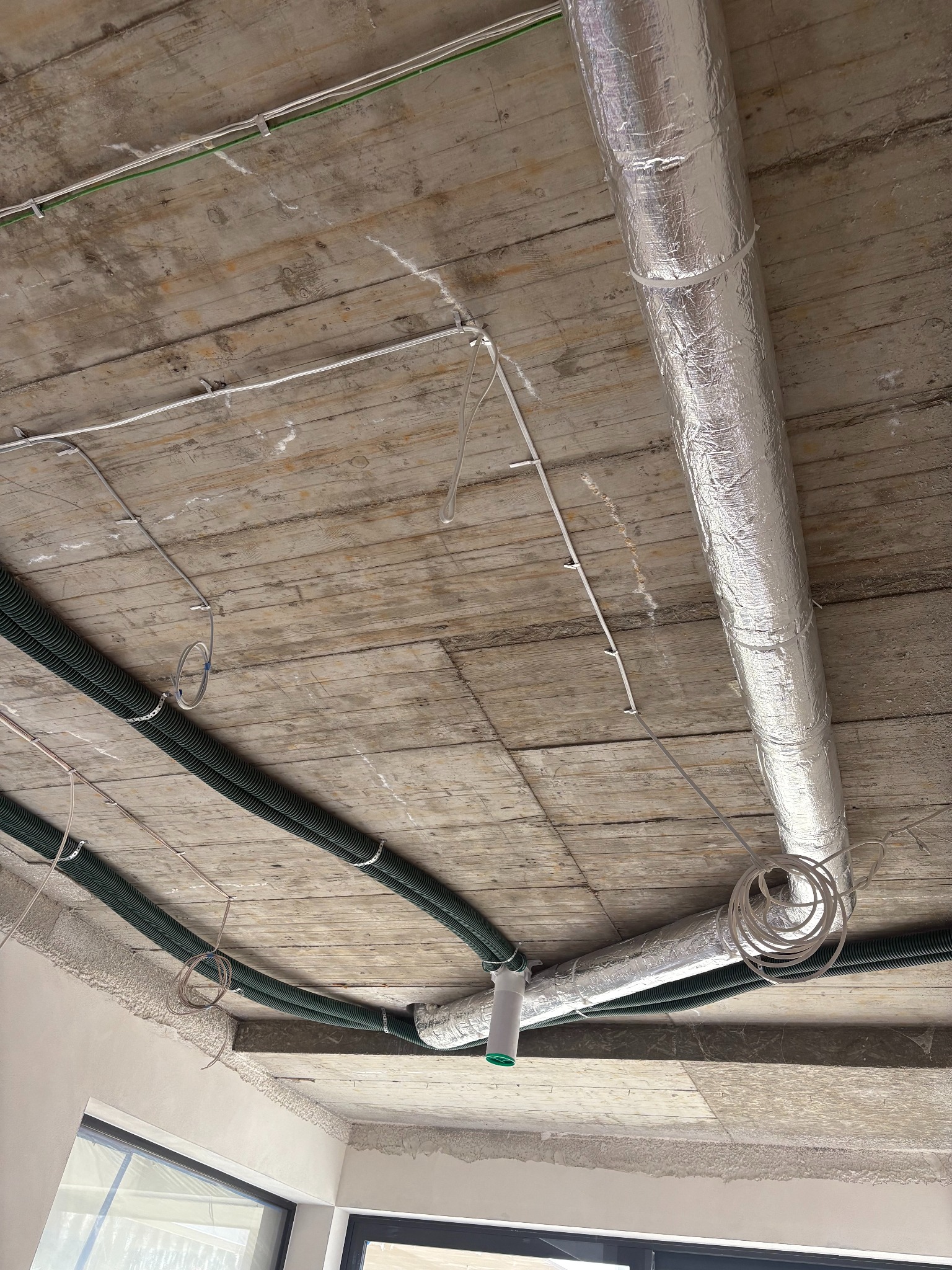 Instalacja wentylacyjna z rurami spiro i przewodami w izolacji, zamontowana pod sufitami w Lublinie. Widoczne kable i elementy mocujące.