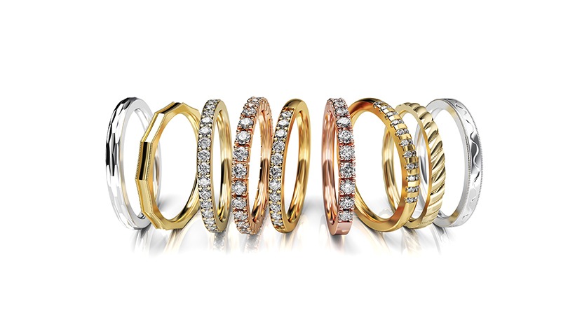 Ekskluzywny zestaw złotych obrączek o różnej fakturze i zdobieniach, w tym z brylantami, ułożonych na białym tle z delikatnym odbiciem.