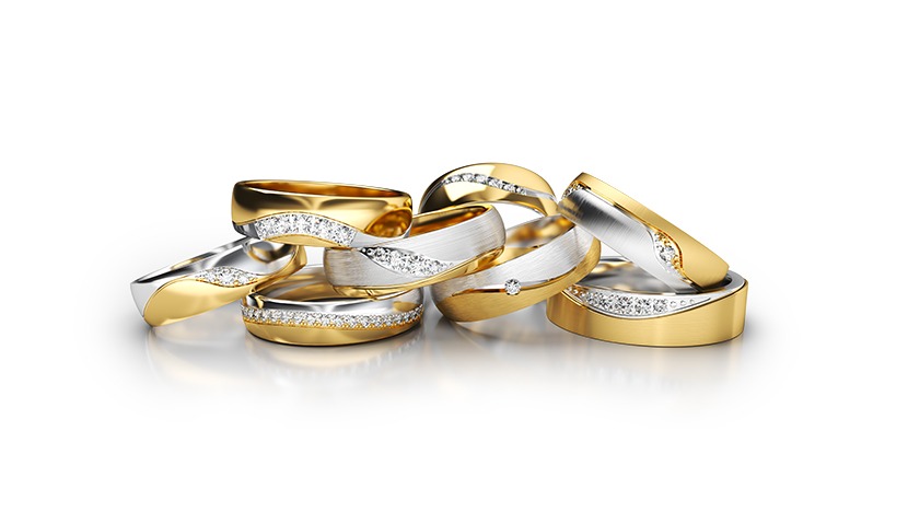 Zestaw złotych i srebrnych obrączek zdobionych cyrkoniami, ułożonych na białym tle z wyraźnym odbiciem. Obrączki ślubne z brylantami.