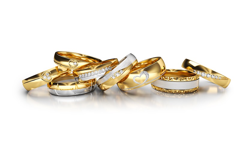 Zestaw złotych obrączek ślubnych z brylantami i motywami serca, ułożonych na białym tle. Obrączki z elementami białego złota i wzorem EKG.