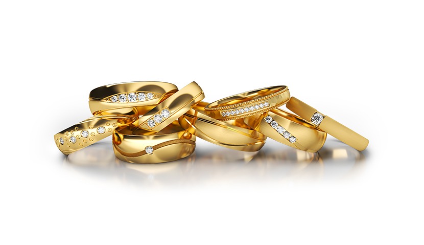 Zestaw złotych obrączek z diamentami o różnych wzorach, ułożonych na białym tle z delikatnym odbiciem, prezentowany w jasnym oświetleniu studyjnym.