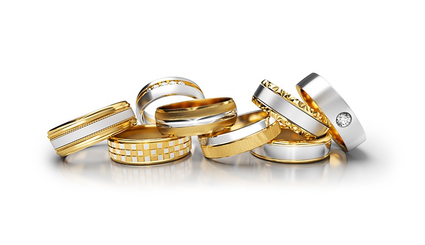 Zestaw siedmiu eleganckich obrączek ślubnych z białego i żółtego złota, o różnych wzorach i wykończeniach, ułożonych na błyszczącej powierzchni w jasnym oświetleniu.