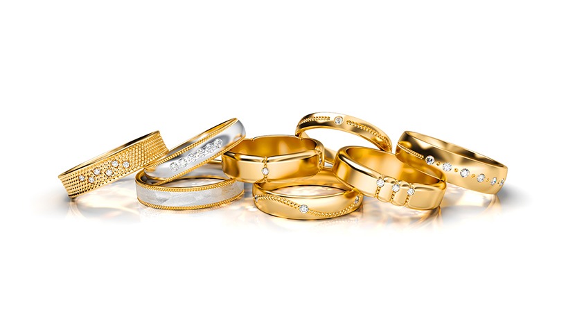 Zestaw złotych obrączek ślubnych z brylantami, o różnych wzorach i wykończeniach, ułożonych na białym tle z delikatnym odbiciem.