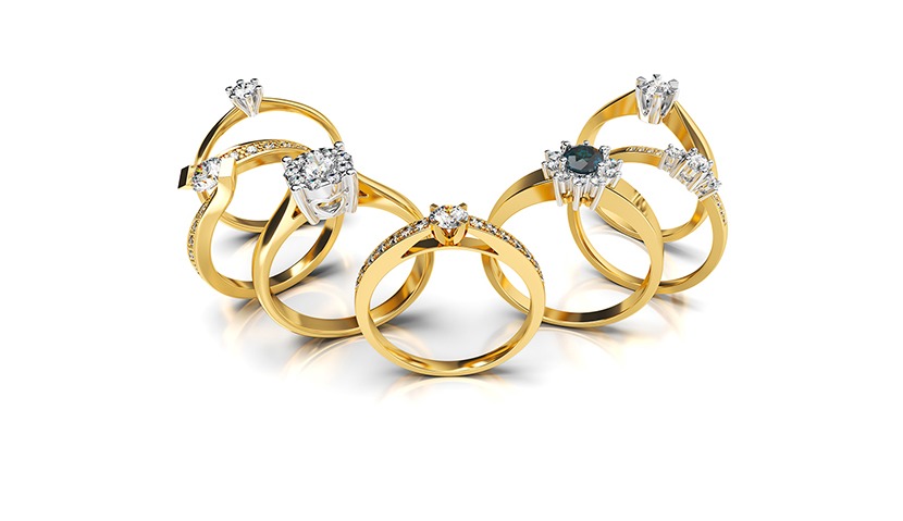 Zestaw złotych pierścionków zaręczynowych z brylantami i kamieniami szlachetnymi, prezentowanych na białym tle z refleksami.