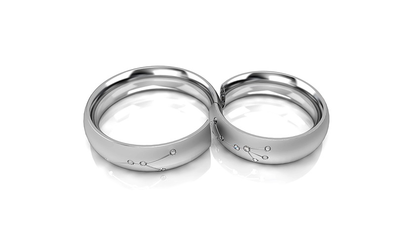 Dwa srebrne pierścionki z motywem konstelacji zdobione drobnymi kamieniami, na białym tle z delikatnym odbiciem, prezentowane w zbliżeniu.