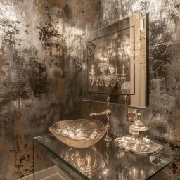 ArtDesign.vip - Elegancka łazienka z umywalką w kształcie liścia na szklanym blacie, lustrem i dekoracyjną tapetą w odcieniach złota i szarości, oświetlona kryształowym żyrandolem.