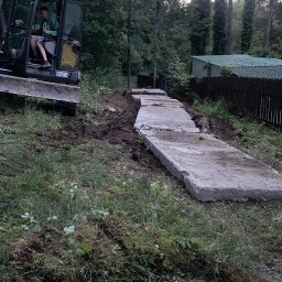 FUNDKOP SP Z O.O. - Żółta koparka ECR50D i ułożone betonowe płyty na ziemi w lesie. Przygotowanie terenu pod budowę, możliwe fundamenty. Operator w kabinie.