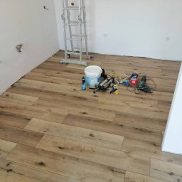 Majstersztyk - Ułożona podłoga z paneli imitujących drewno w jasnym wnętrzu. Widoczne narzędzia i drabina. Świeżo położona podłoga w trakcie prac wykończeniowych.
