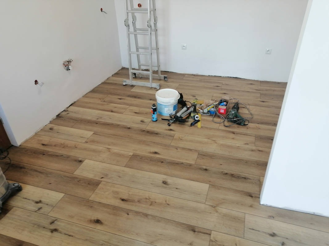 Ułożona podłoga z paneli imitujących drewno w jasnym wnętrzu. Widoczne narzędzia i drabina. Świeżo położona podłoga w trakcie prac wykończeniowych.