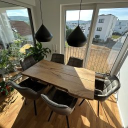 Drewniane Klimaty - Stół z blatem z litego drewna o nieregularnych krawędziach, otoczony sześcioma krzesłami w nowoczesnym wnętrzu z dużymi oknami i widokiem na zieleń.