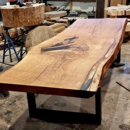 Drewniane Klimaty - Wyjątkowy blat drewniany z żywicą epoksydową, osadzony na metalowych nogach. Widoczne słoje drewna i naturalne krawędzie. W tle warsztat stolarski.