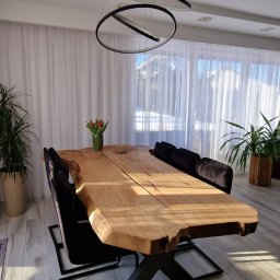 Drewniane Klimaty - Stół z blatem z litego drewna o nieregularnych krawędziach, na metalowej podstawie w kształcie litery X. Nad stołem nowoczesna lampa z okręgów.