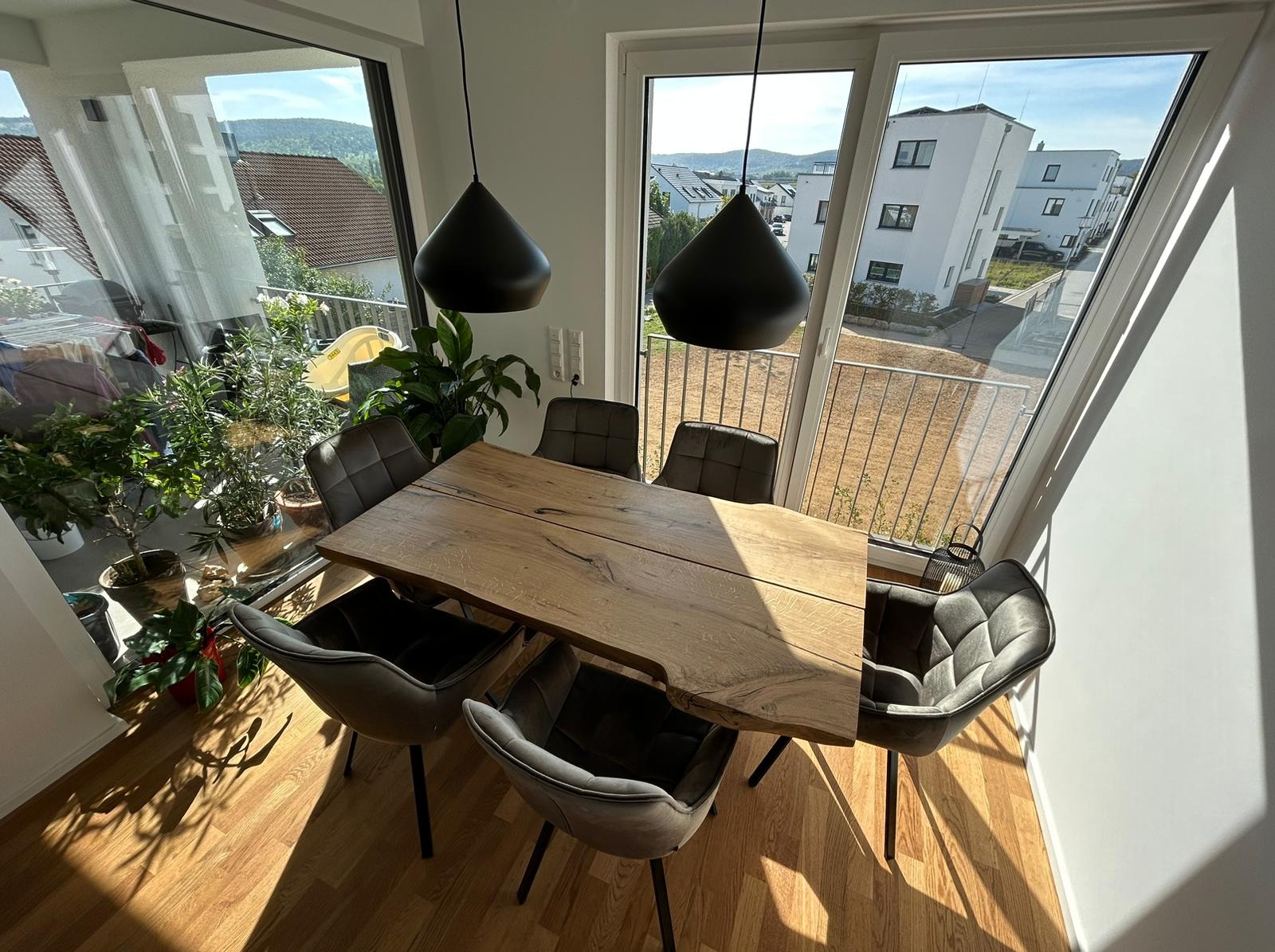 Stół z blatem z litego drewna o nieregularnych krawędziach, otoczony sześcioma krzesłami w nowoczesnym wnętrzu z dużymi oknami i widokiem na zieleń.