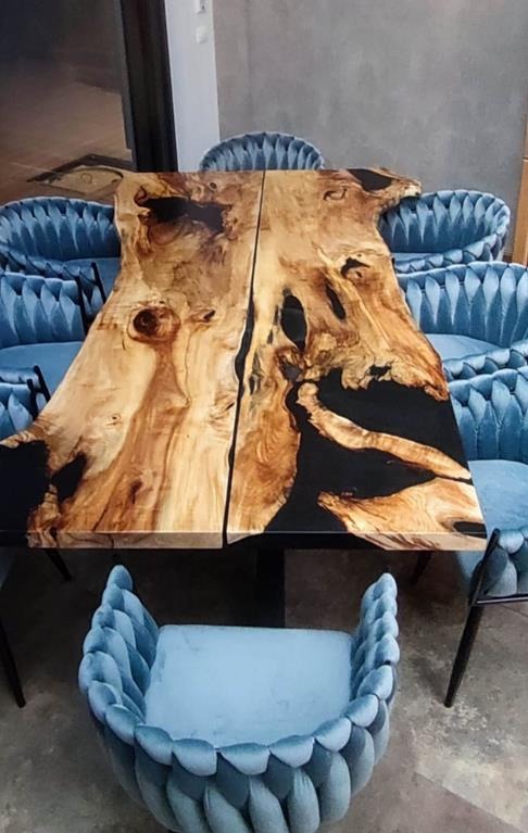 Stół z dwuczęściowego blatu z żywicą epoksydową, otoczony błękitnymi krzesłami w stylu glamour. Blat z naturalnego drewna o nieregularnych krawędziach.