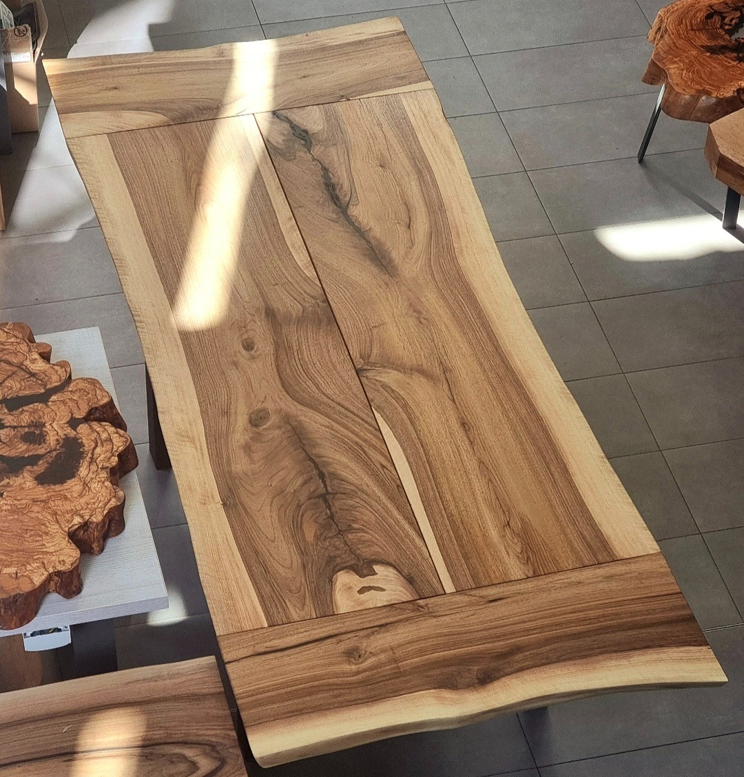 Stół z drewna orzechowego, z widocznym usłojeniem i naturalnymi krawędziami. Dwie deski połączone w jedną całość, wykończone na gładko. Dekoracyjne detale z drewna.