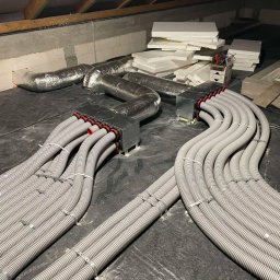 Budotom Pompy Ciepła - Rozprowadzenie instalacji rekuperacji w budynku, widoczne liczne elastyczne rury wentylacyjne w kolorze szarym, połączone z centralą wentylacyjną.