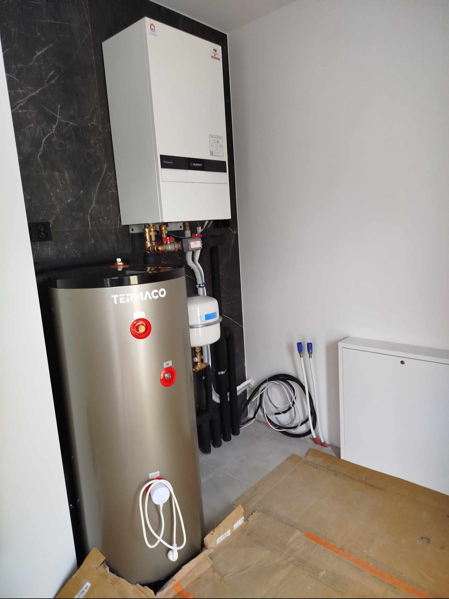 Zamontowany bojler Termaco z piecem gazowym Buderus na ścianie z marmurowym wzorem, widoczne rury i kable.