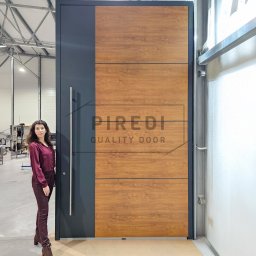 Piredi - Wysokie drzwi zewnętrzne z drewnianym panelem i stalowym uchwytem, obok których stoi kobieta. Nowoczesny design i duże rozmiary.