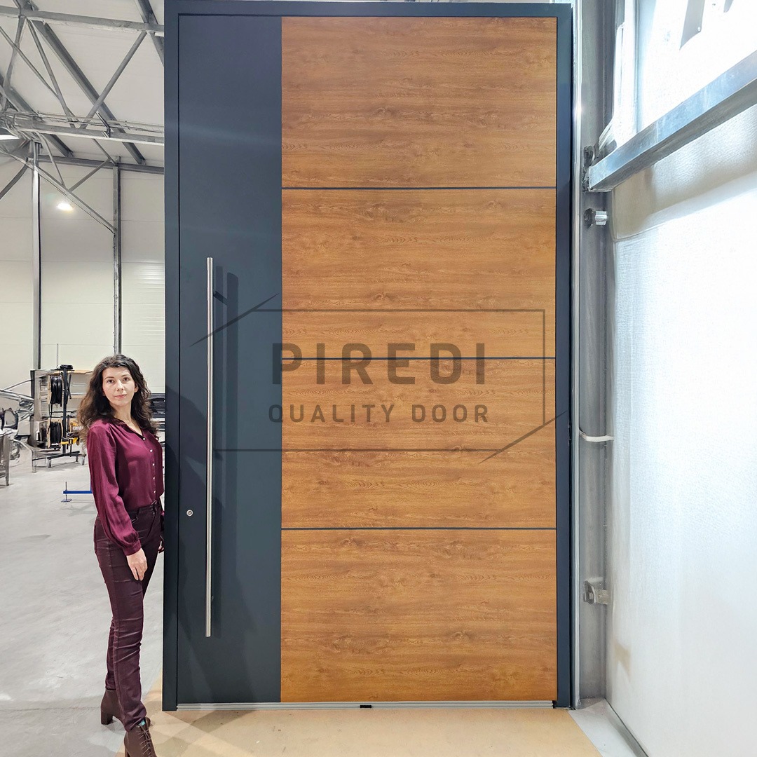 Wysokie drzwi zewnętrzne z drewnianym panelem i stalowym uchwytem, obok których stoi kobieta. Nowoczesny design i duże rozmiary.