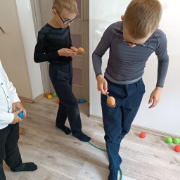 AniBajka - Dzieci w trakcie zabawy: przenoszenie jajka na łyżce, balansowanie, kolorowe piłki rozsypane na podłodze, elementy wyposażenia wnętrza.