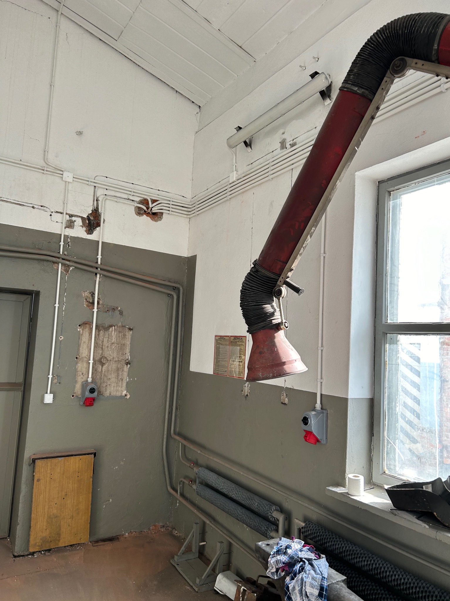 Szare wnętrze warsztatu w Borkach z widocznymi przewodami elektrycznymi na ścianie, lampą i instalacją odciągową. Widoczne gniazda i przełączniki.