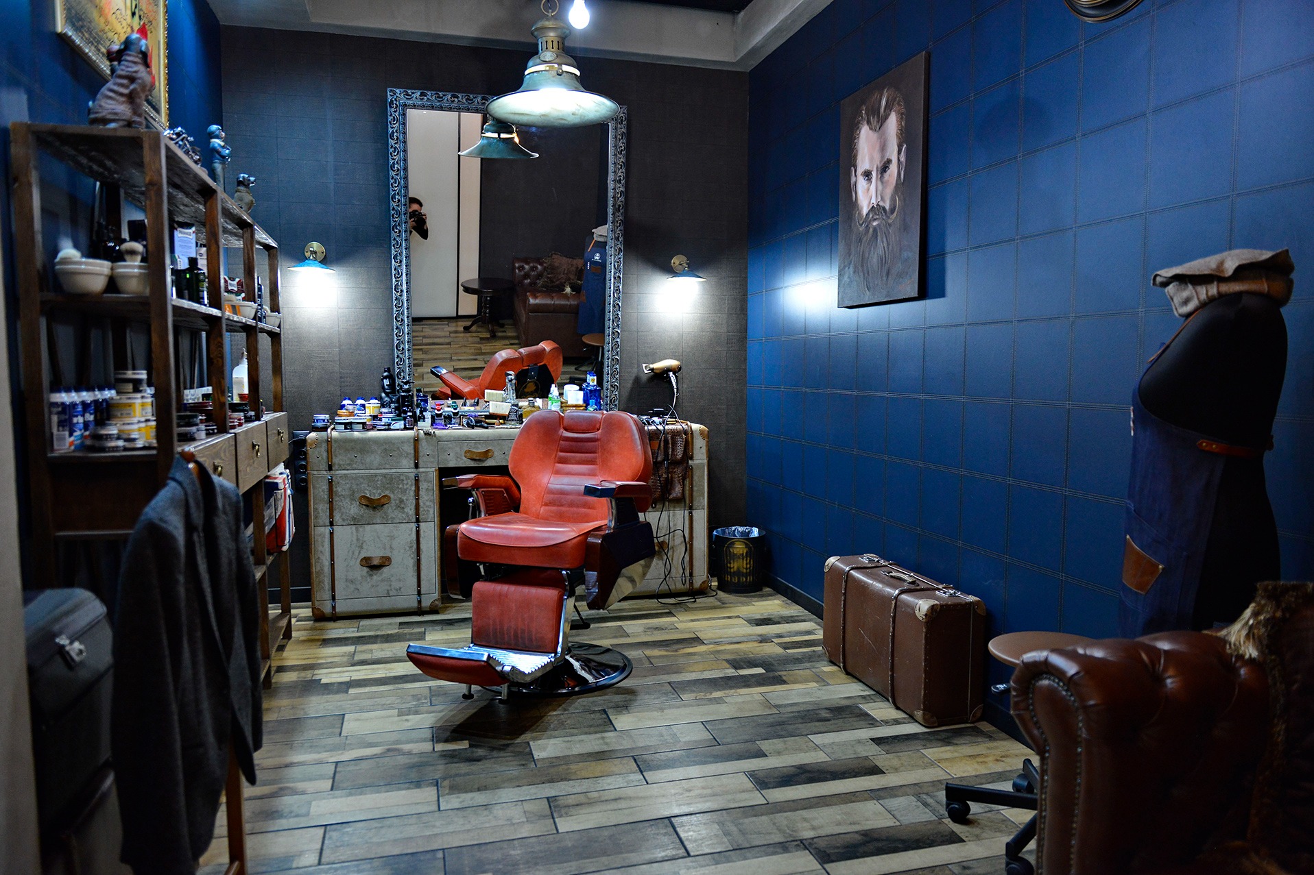 Wnętrze barbershopu: czerwony fotel fryzjerski, lustro z odbiciem fotografa, niebieskie ściany w kratkę, drewniane podłogi i vintage'owe akcenty.