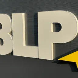 Zewnętrzny szyld 3LP z żółtą strzałką na szarej, poziomo żebrowanej elewacji, widoczny w ukośnym ujęciu z dołu, w jasnym oświetleniu.