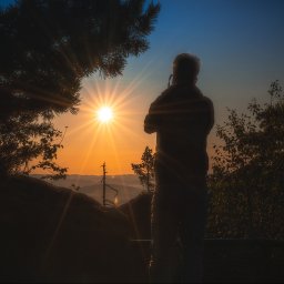 Adrian Ekiert Fotografia - Sylwetka osoby podziwiającej wschód słońca z górskim krajobrazem w tle, uchwycona z niskiego kąta, z elementami roślinności w kadrze.