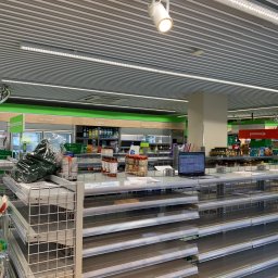 Mistre Group sp. z o.o. - Wnętrze sklepu z pustymi regałami i oświetleniem LED. Widoczny sufit z rastrową konstrukcją i elementy wyposażenia sklepowego w odcieniach szarości i zieleni.