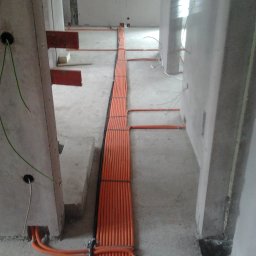 Mistre Group sp. z o.o. - Pomarańczowe kable elektryczne ułożone w rzędach na podłodze w surowym stanie, prowadzone wzdłuż ścian i filarów w trakcie instalacji.
