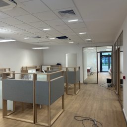 Mistre Group sp. z o.o. - Jasne biuro po remoncie: nowe podłogi, ścianki działowe, oświetlenie sufitowe. Widoczne ślady prac wykończeniowych i sprzęt.