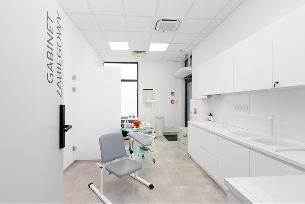 Wnętrze jasnego gabinetu zabiegowego z białymi meblami, krzesłem dla pacjenta i napisem 'Gabinet Zabiegowy' na drzwiach. Minimalistyczny design, nowoczesne oświetlenie.