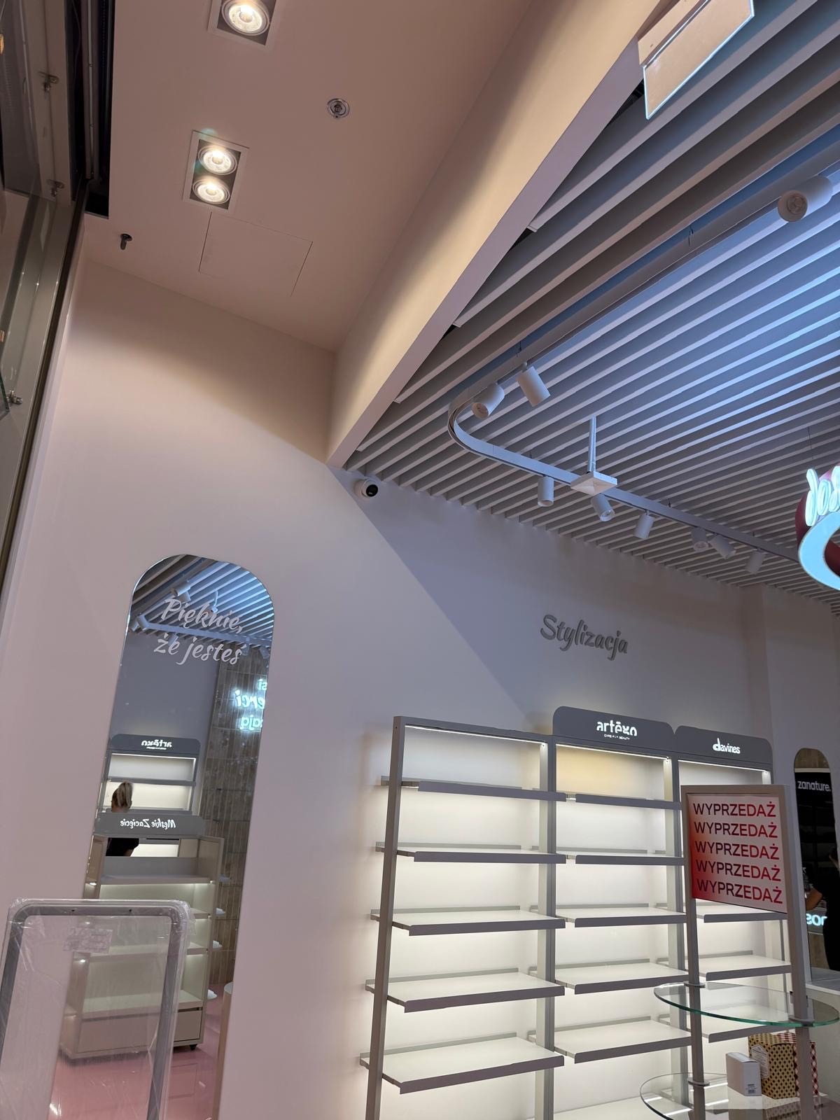 Nowoczesne oświetlenie sufitowe w sklepie z półkami ekspozycyjnymi. Widoczne reflektory i listwy LED. Minimalistyczny design wnętrza sklepowego.