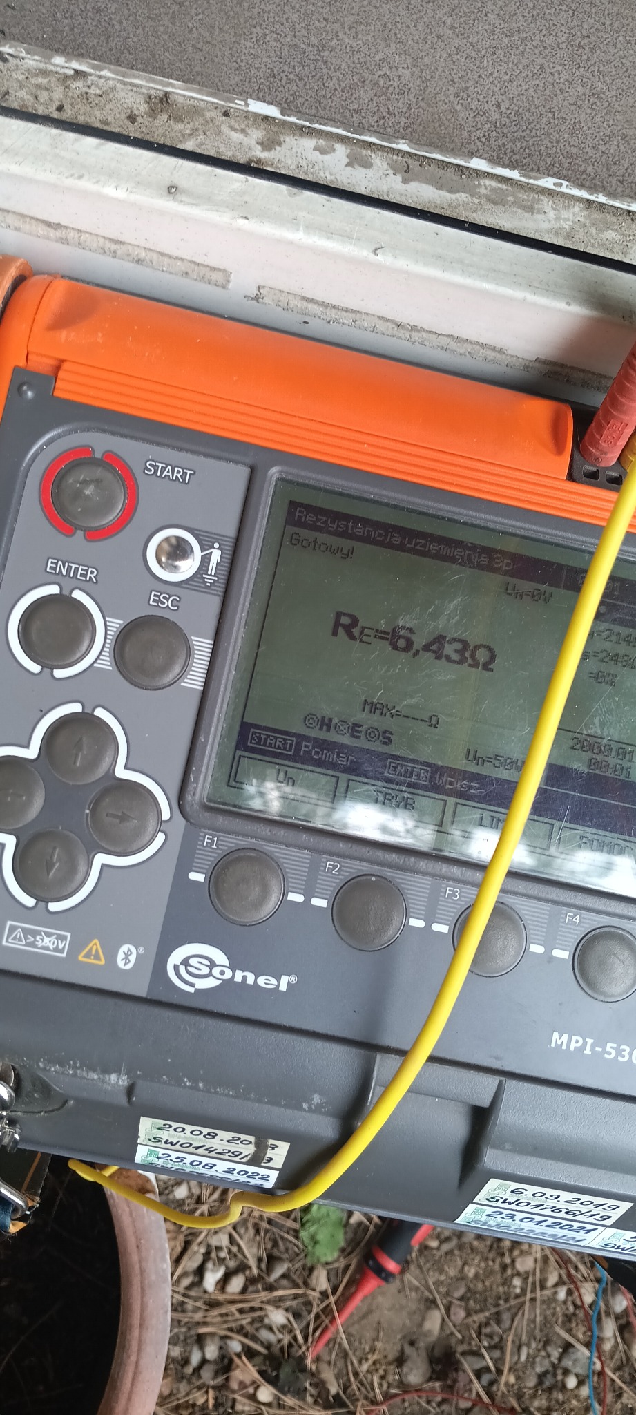 Miernik Sonel MPI-530 z żółtym przewodem, wskazujący rezystancję uziemienia 6,43 Ω. Widoczne przyciski i ekran urządzenia. Pomiar elektryczny w trakcie realizacji.
