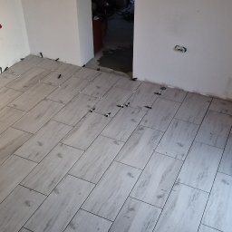 Adrian Tomczyk - Ułożone płytki podłogowe imitujące drewno z krzyżykami dystansowymi w trakcie prac wykończeniowych w Radomiu. Widoczny fragment ściany z instalacją.