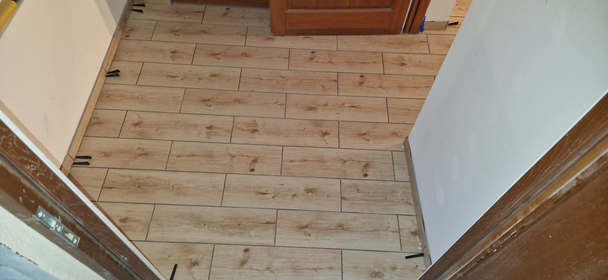 Ułożone panele podłogowe imitujące drewno w jasnym odcieniu, z widocznymi krzyżykami dystansowymi. Ujęcie z perspektywy wejścia do pomieszczenia.