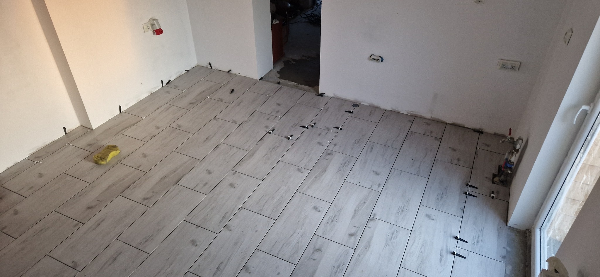 Ułożone płytki podłogowe imitujące drewno z krzyżykami dystansowymi w trakcie prac wykończeniowych w Radomiu. Widoczny fragment ściany z instalacją.