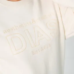 Kremowa bluza z beżowym, delikatnym haftem 'DIAS aesthetics&comfort Est.2010', widoczna na osobie od szyi w dół. Minimalistyczny design.