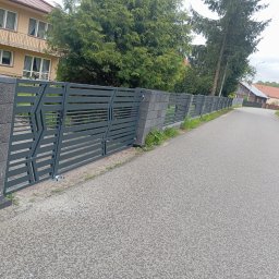 KRIS-STAL - Nowoczesne ogrodzenie panelowe z szarymi, betonowymi słupkami i metalowymi przęsłami o geometrycznym wzorze, widoczne z perspektywy ulicy.